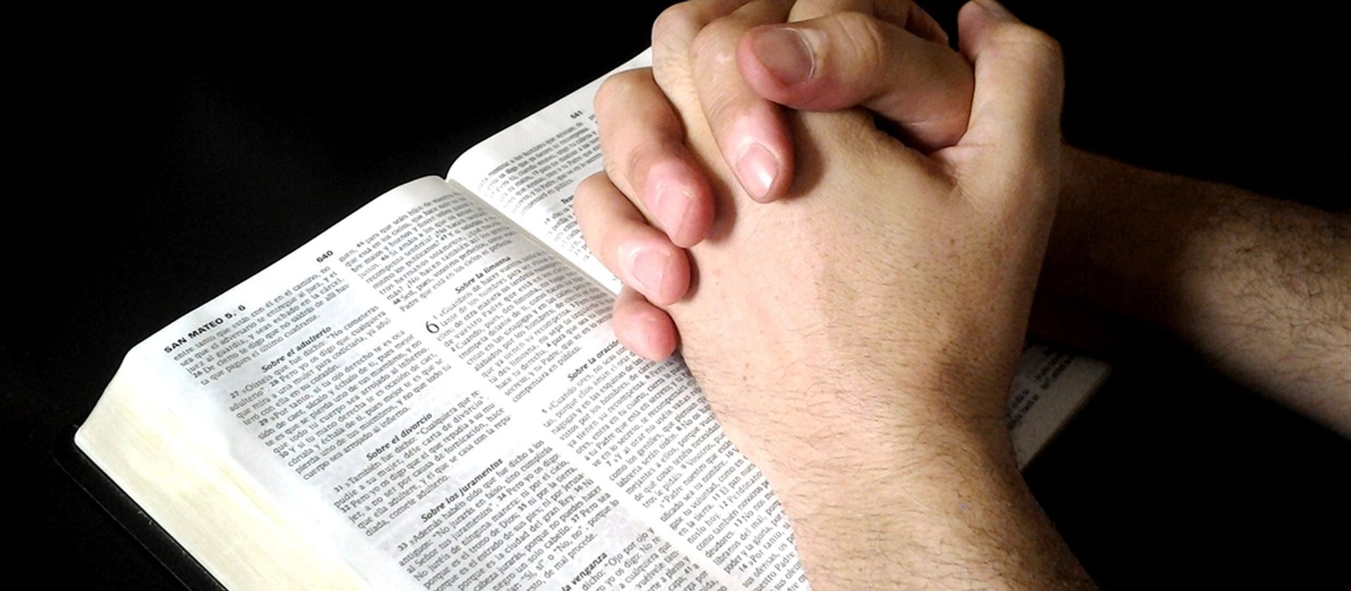 Hands folded in prayer upon an open Bible